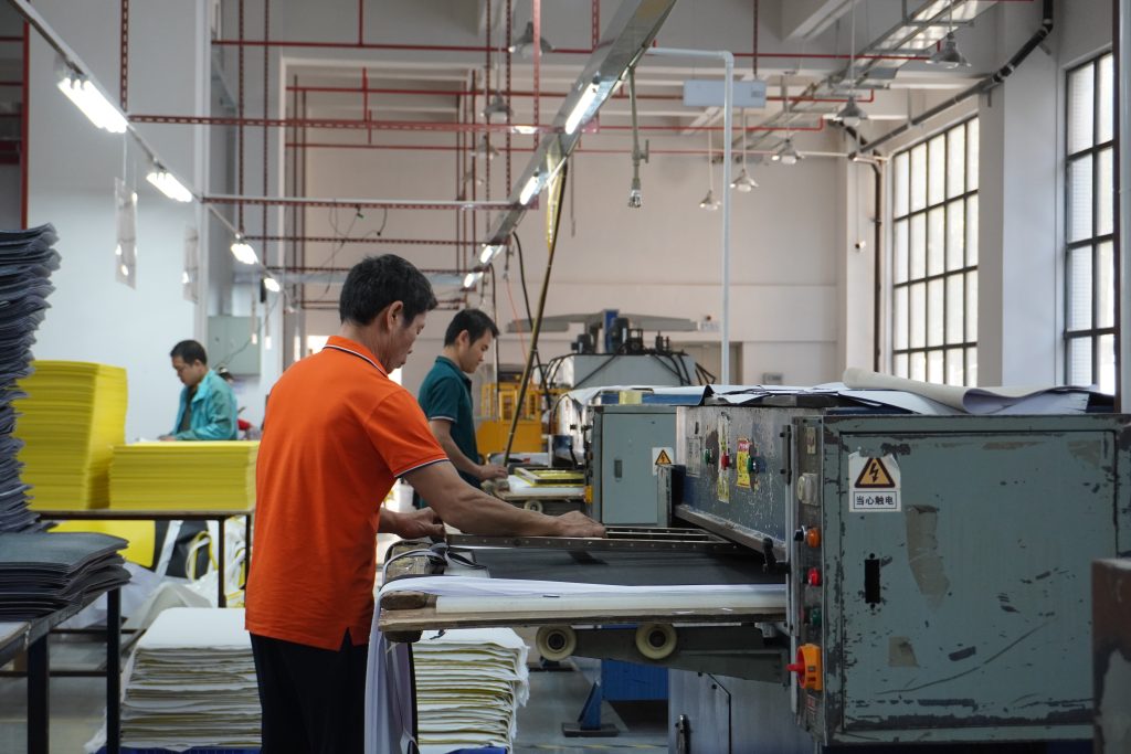 Worker operating cutting machine for precise mouse pad production in professional manufacturer's workshop.