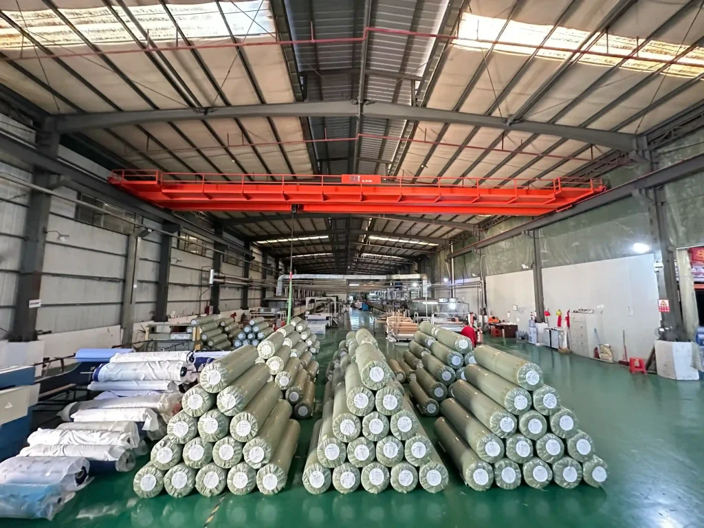 Neatly stacked finished rubber mat and mouse pad rolls in a spacious industrial warehouse, showcasing Padmat Rubber's large inventory and organized production output for global B2B orders.